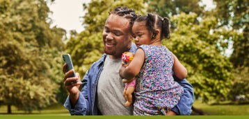 An individual using their phone while carrying their child outside.