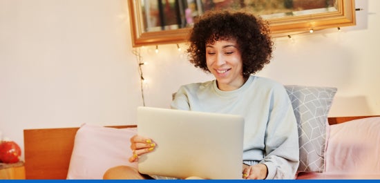 A smiling individual using their laptop while sitting down.